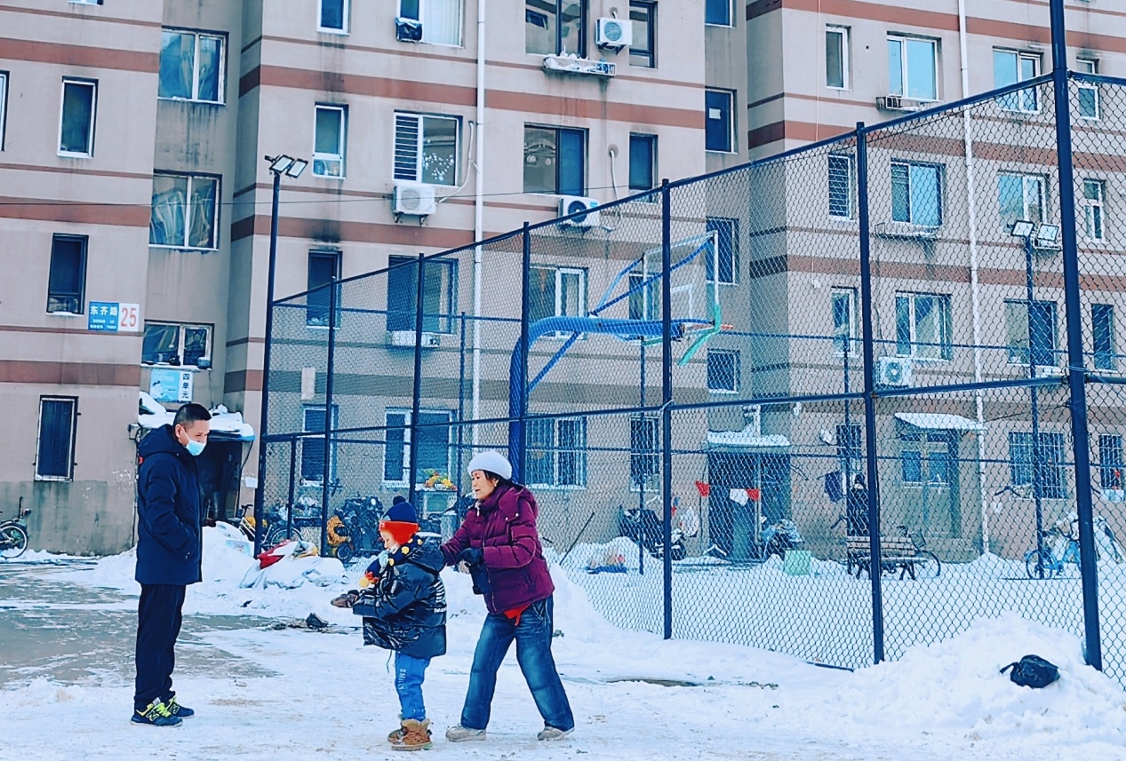 丹东市振安区珍珠街道的老旧小区居民楼被粉刷一新，雪后初晴，在瑞雪的装点下格外亮眼，在东齐路25号楼门前，相遇的邻居们热情地唠着家常。（摄影：王卢莎）