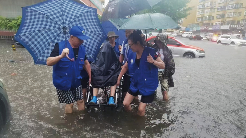 8月16日，暴雨导致道路积水。元宝区兴东街道虹桥社区网格员冒雨涉水，合力抬起轮椅，护送行动不便的群众安全通过积水路段。张怡媛 摄