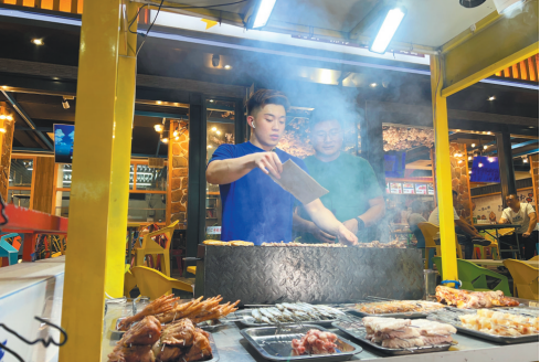 锦州烧烤非物质文化遗产传承人李政焱（左）正在烹饪美食。