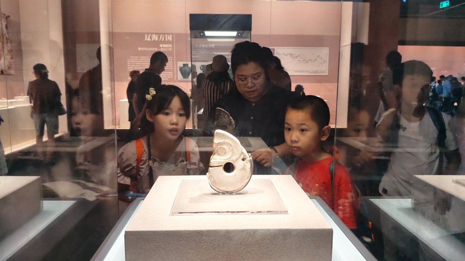 暑假期间，一位家长带孩子欣赏辽博展品玉猪龙。